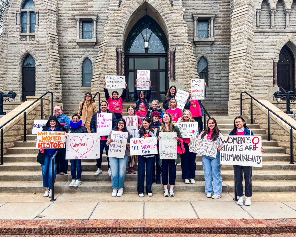 A group of women with signs from their march pose in front of St. John's Church