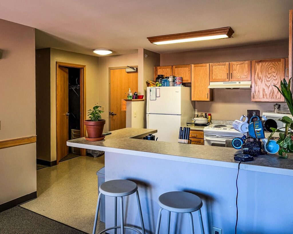 A picture of an Opus Hall dormitory showing a countertop with stools in foreground and an open-concept kitchen behind.