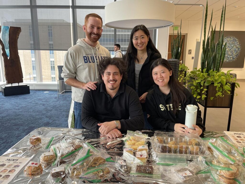 Four people pose behind a table full of baked goods.