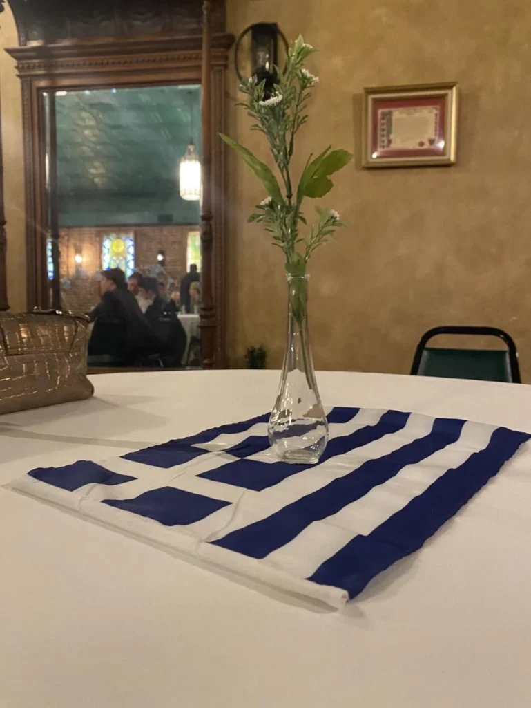 A Greek Flag with a flower and vase on top of it adorns tables
