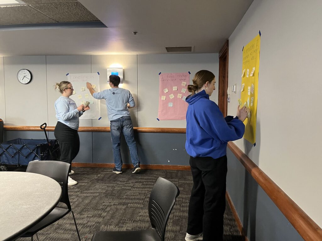 Students stand and put sticky notes on posters around a room.
