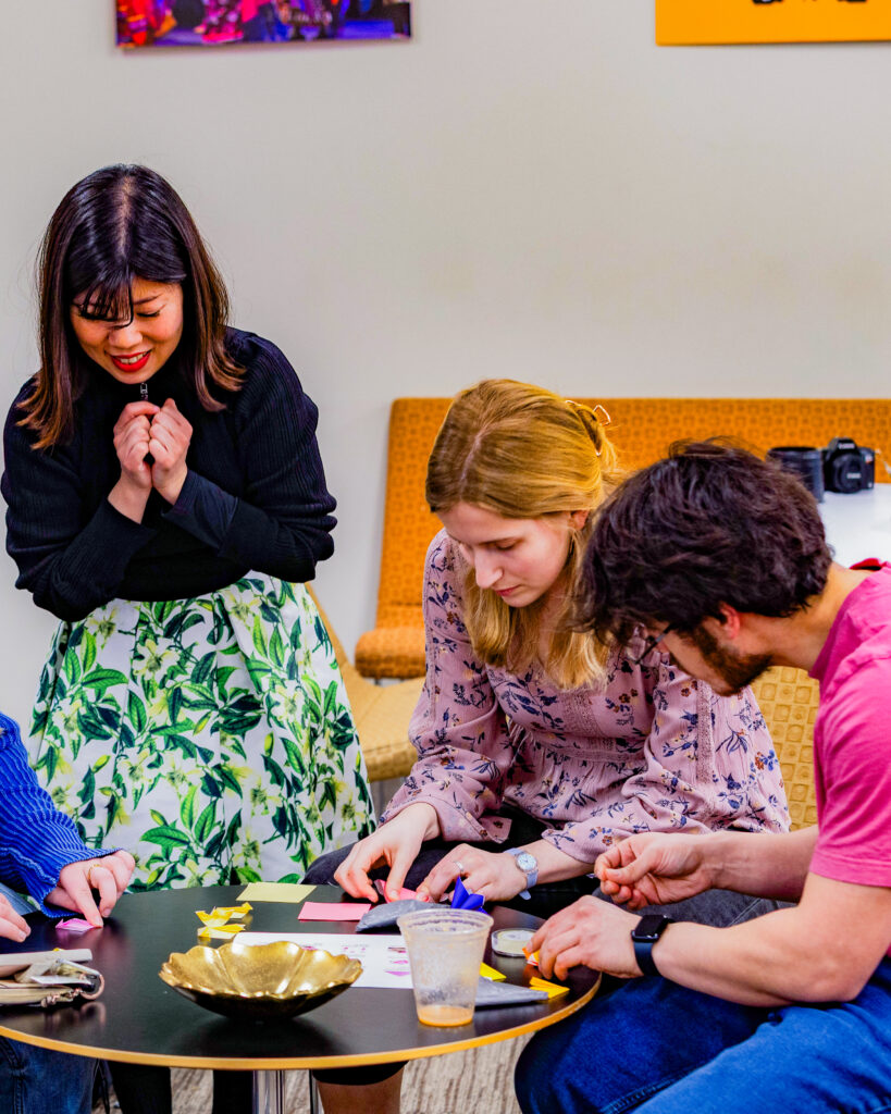 Mana Nakano helps students, including Allison Benjamin (center) and Lucio Perez (right), fold their origami flowers during this monthβs Take Time Tuesday event hosted by the CIC.